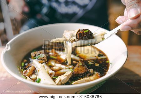 Close Up Guay Jub, Gravy Noodle Soup  Thai Street Food On Wooden Table With Hand And Fork