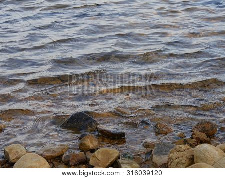 Close Up Of Water Flowing Gently To A Rocky Shoreline Of A Lake