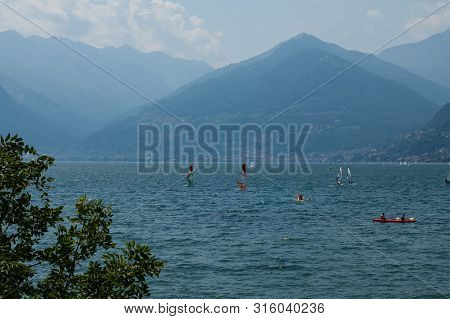 Lake Como, Italy - July 21, 2019: View Of Mountain Lake On A Sunny Summer Day. Windsurfers And A Boa