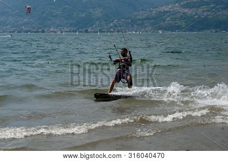 Lake Como, Italy - July 21, 2019. Water Sport: Kitesurfer Riding On A Bright Sunny Summer Day Near T