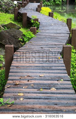 Wooden Walkpath Above Green Garden And By The River.