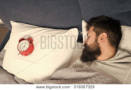 Man Bearded Hipster Sleepy Face In Bed With Alarm Clock. Problem With Early Morning Awakening. Get U