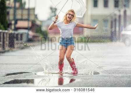 Cheerful Girl Jumping With White Umbrella In Dotted Red Galoshes. Hot Summer Day After The Rain Woma