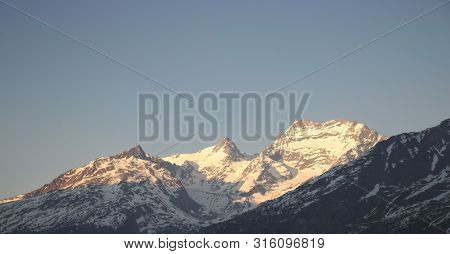 Last Rays Of Sun Illuminate The Mountains Covered With Snow At Evening