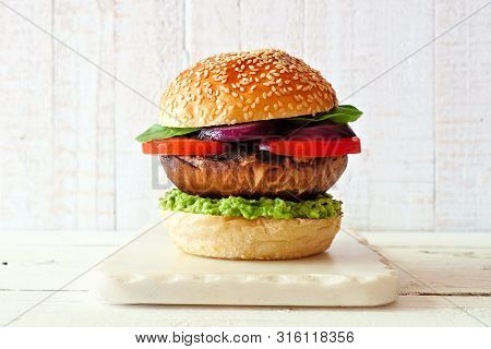 Portobello Mushroom Meatless Burger With Avocado, Tomato, Spinach And Onion On A Marble Serving Boar