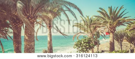 Toned Photo Of Puerto Del Carmen Beach In Lanzarote, Canary Islands, Spain. Blue Sea, Palm Trees, Se