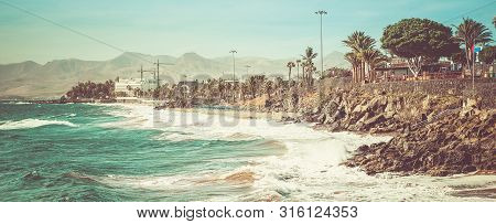 Toned Photo Of Puerto Del Carmen Beach In Lanzarote, Canary Islands, Spain. Blue Sea, Palm Trees, Se