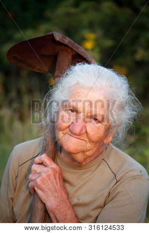 Close-up Portrait Of An Old Woman With Gray Hair Smiling And Looking At The Camera, Holding A Rusty