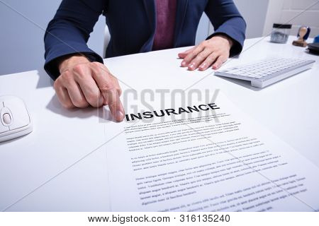 Mid Section Of A Businessman Showing Insurance Document Over White Desk At Office
