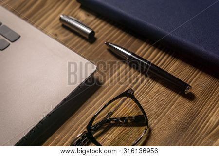 Notebook, Laptop, Glasses And Pen On The Table.