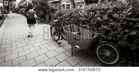 Haarlem, Netherlands - Aug 16, 2018: Rear View Of Woman With Backpack Walking On Tiny Street With Pa