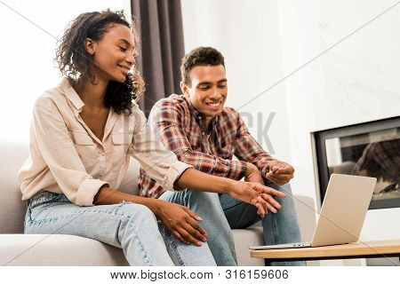 African American Couple Sitting On Sofa And Looking At Laptop While Man Holding Credit Card And Woma