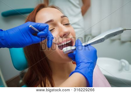 Young Beautiful Woman With Beautiful White Teeth Sitting On A Dental Chair. Dentist Examining A Pati