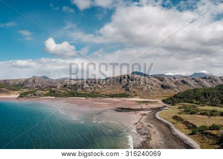 A Deserted Sandy Beach And Turquoise Sea At Gruinard Bay With Snow Capped Hills In The Distance On T