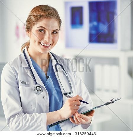 Young Woman Doctor Is Standing With Board With Clipboard Smilin