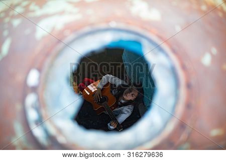 A Young Woman Sits And Plays Guitar Inside Of Old Abandoned Ship. View Through The Ship Porthole.