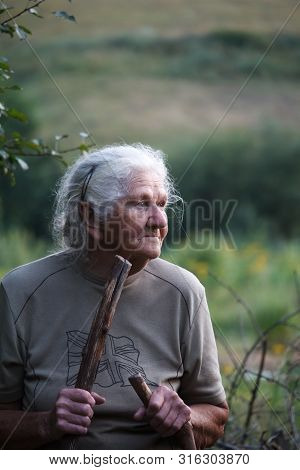 Portrait Of An Old Woman With Arthritic Feet Walking In A Grassy Meadow Leaning On A Stick As A Cane