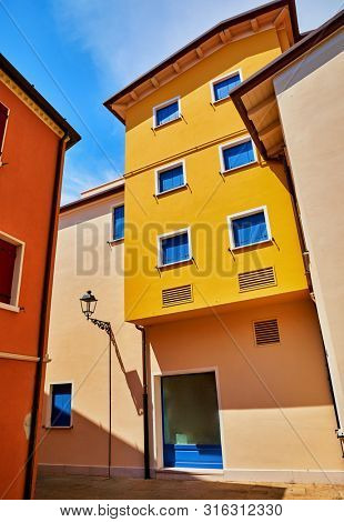 Caorle, Italy. Mediterranean resort town. Motley coloured houses with windows and street lamp at narrow bright sunny summer day with blue sky.