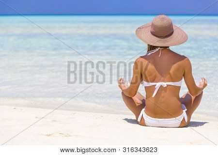 Young Lady Sitting On The Shore In Maldives With Straw Hat Meditating.