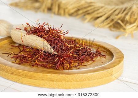 Lot Of Whole Dry Shaffron Thread On Bamboo Plate With Wooden Scoop And Jute Cloth On White Wood