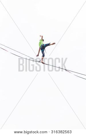 A Man Is Walking Along A Stretched Sling. Highline On The Background Of The Cloudy Sky. The Man Has 