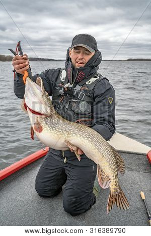 Pike Fishing. Happy Fisherman With Big Fish Trophy At The Boat With Tackles