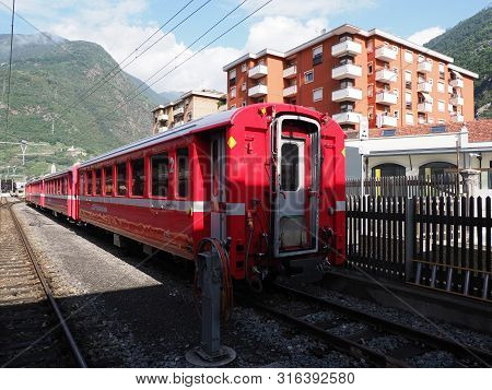 Tirano, Italy On August 2018: Side Of Rhaetian Railway Train On Station And Housing Estate In Europe