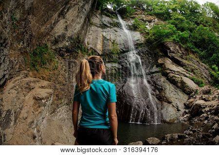 Female Tourist In Sportswear Standing Near Waterfall