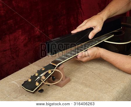 Musical Instrument Guitar Repair And Service - Worker Grinds Black Guitar Neck Frets.
