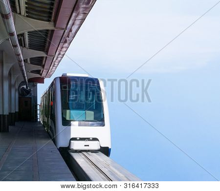 Monorail Train Departs From Platform Of Railway Station Against Blue Sky Background. Copy Space