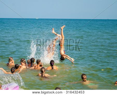 Odesa Rgn. Ukraine, July 29, 2018: A Young Man Throws Up A Girl In The Sea, And She Jumps Into The W