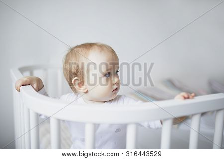 Adorable Baby Girl In Co-sleeper Crib Attached To Parents Bed. Little Kid Sitting In Cot
