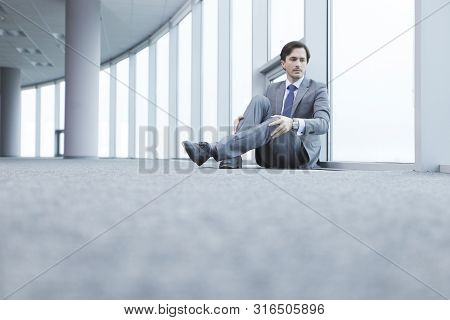 Businessman Sitting On Floor In Office Near Window