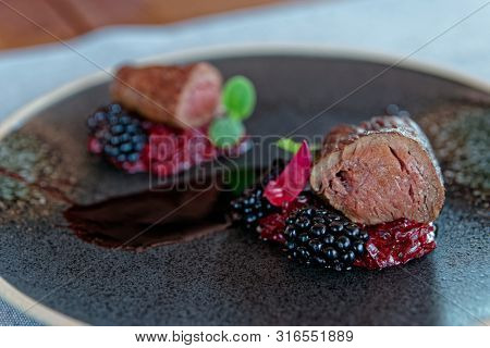 Venison fillet with beetroot carpaccio and blackberries on dark plate, close-up shot
