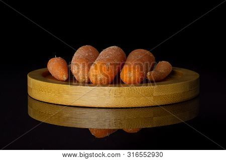 Group Of Five Whole Stale  Orange Stale Baby Carrot Baby On Bamboo Plate Isolated On Black Glass