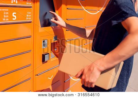 Man Using Automated Self Service Post Terminal Machine Or Locker To Deposit The Parcel For Storage