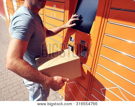Man Using Automated Self Service Post Terminal Machine Or Locker To Deposit The Parcel For Storage