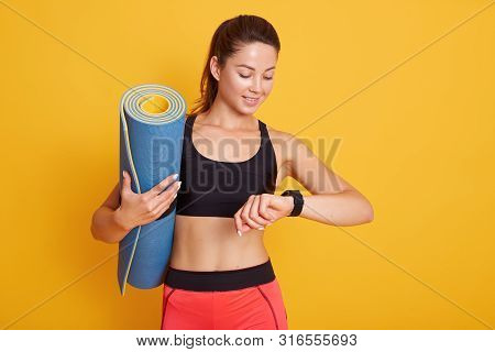 Horozontal Shot Of Fitness Woman After Workout Session Checks Results On Smartwatch In Fitness App, 