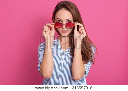Portrait Of Fashion Attractive Woman Peeking Over Sunglasses. Female Model Posing Against Pink Studi