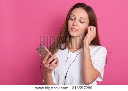 Attarctive Female Putting Earphones In Ears. Portrait Of Pleased Relaxed Attractive Dreamy Girl With
