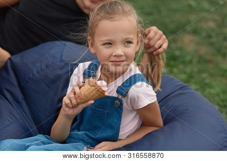 Adorable Kid Girl Holding Ice Cream In Hands, Sitting Next To Fathe On Farameless Chair Outdoor, Fat