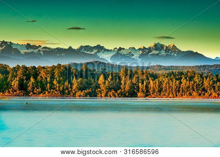 Dramatic Light On The Peaks Of The Southern Alps Behind The Forest And Okarito Lagoon