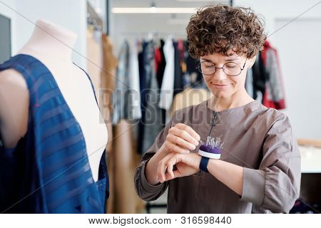 Young tailor taking pin from pincushion on her wrist during work