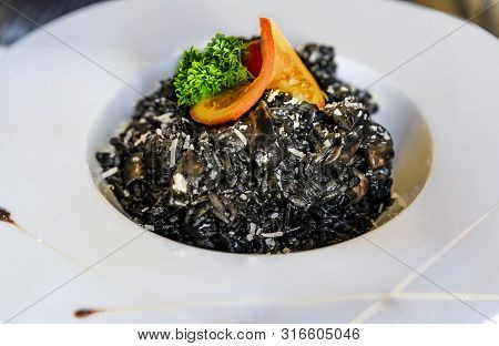 Squid Ink Black Risotto With Squid Rings Sprinkled With Parmesan, Served With A Slice Of Orange And 