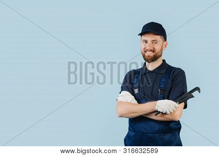 Happy Service Worker With Hands Crossed Holding Adjustable Spanner In The Hand. He Is Dressed In Dar