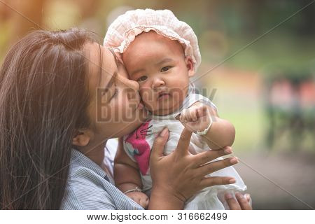 Young Beautiful Asian Mother Holding And Kissing Her Daughter Outdoor.