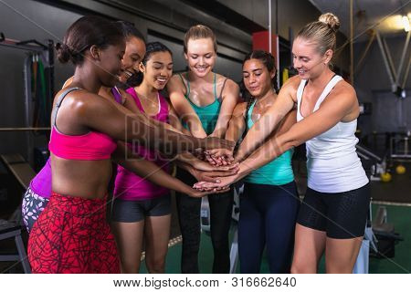 Front view of diverse female athletic team forming hand stack in fitness center. Bright modern gym with fit healthy people working out and training