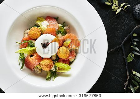 Beautiful Restaurant Plate of Trout Fillet 48 Degrees and Egg Poached with Warm Potatoes Top View. Exquisite Italian Arancino and Smoked Salmon or Sliced Red Fish on Natural Black Marble Background