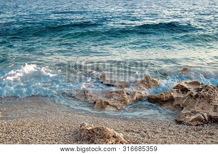 Rocky Beach And Crystal Turquoise Water Of Ionian Sea In Albania. Calm And Relaxing View With Flower