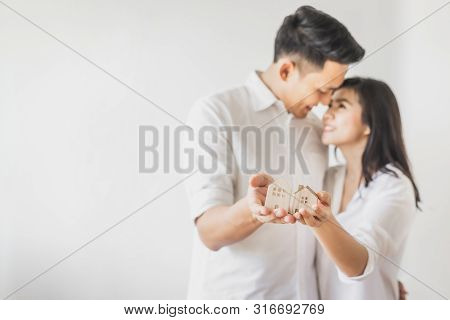 Happy Asian Couple In Love Showing Wooden House Model. Moving To New House Or Strating New Family Li